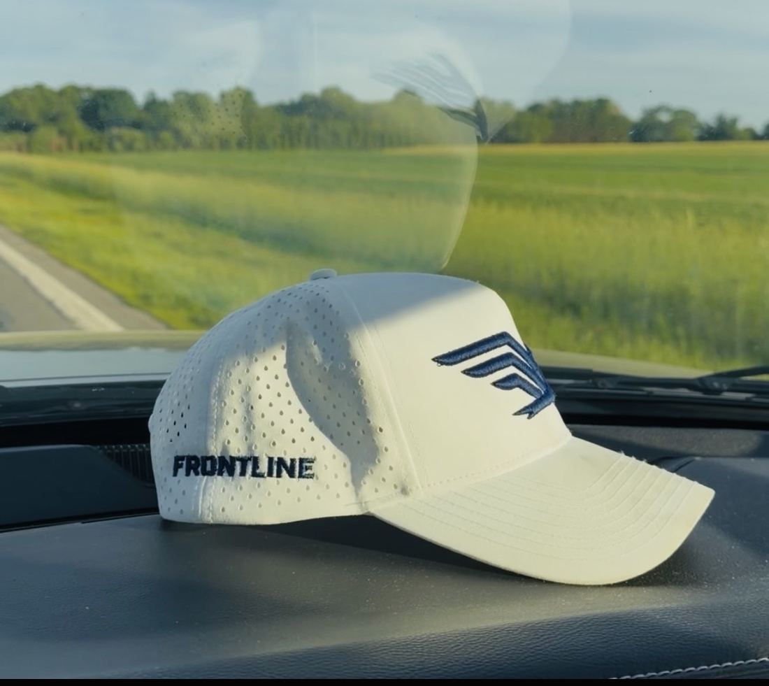 A white Frontline hat on a truck dashboard with open fields ahead