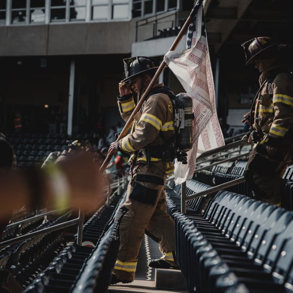 Firefighters in full gear carrying an American flag up the stadium stairs at a memorial stair climb